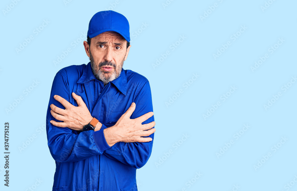 Middle age handsome man wearing mechanic uniform shaking and freezing for winter cold with sad and shock expression on face Middle age handsome man wearing mechanic uniform shaking and freezing for winter cold with sad and shock expression on face