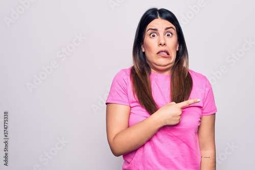 Young beautiful brunette woman wearing casual pink t-shirt standing over white background Pointing aside worried and nervous with forefinger, concerned and surprised expression