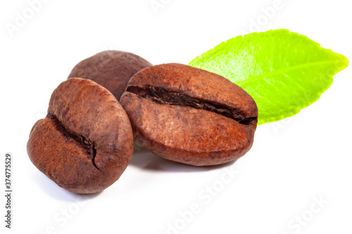 three roasted coffee beans and a green leaf on a white background, isolate