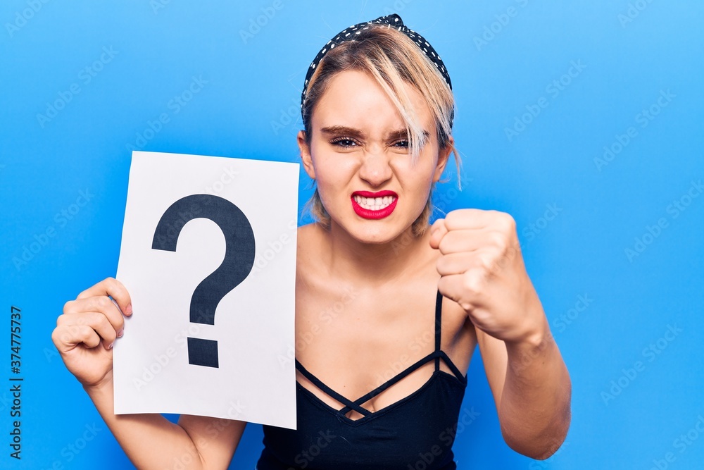 Young beautiful blonde woman holding question mark annoyed and frustrated shouting with anger, yelling crazy with anger and hand raised Young beautiful blonde woman holding question mark annoyed and frustrated shouting with anger, yelling crazy with anger and hand raised