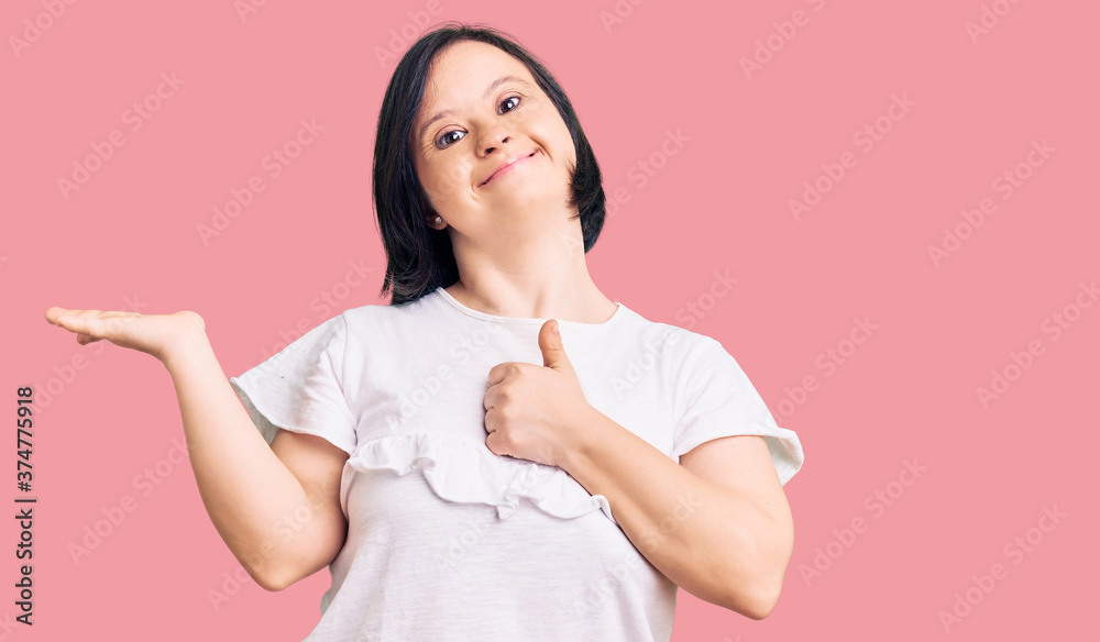 Brunette woman with down syndrome wearing casual white tshirt showing palm hand and doing ok gesture with thumbs up, smiling happy and cheerful