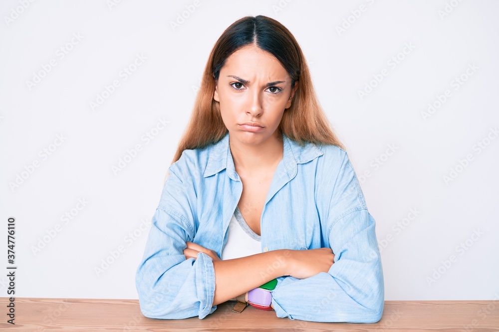 Young brunette woman sitting on the table wearing casual clothes skeptic and nervous, disapproving expression on face with crossed arms. negative person. Young brunette woman sitting on the table wearing casual clothes skeptic and nervous, disapproving expression on face with crossed arms. negative person.