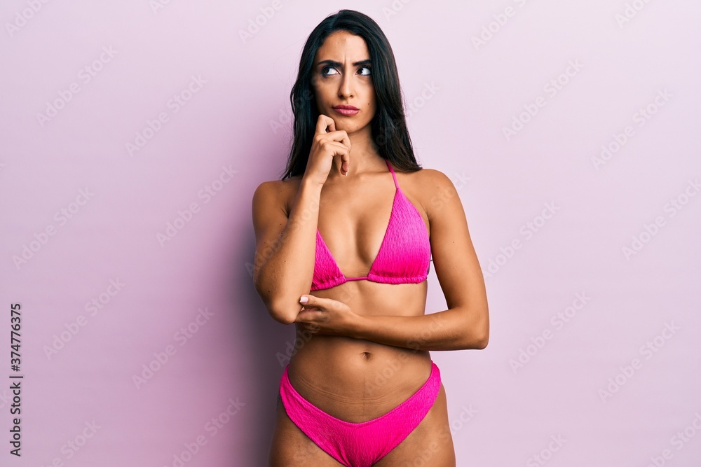Fototapeta premium Beautiful hispanic woman wearing bikini serious face thinking about question with hand on chin, thoughtful about confusing idea
