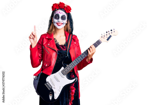 Woman wearing day of the dead costume playing electric guitar surprised with an idea or question pointing finger with happy face, number one