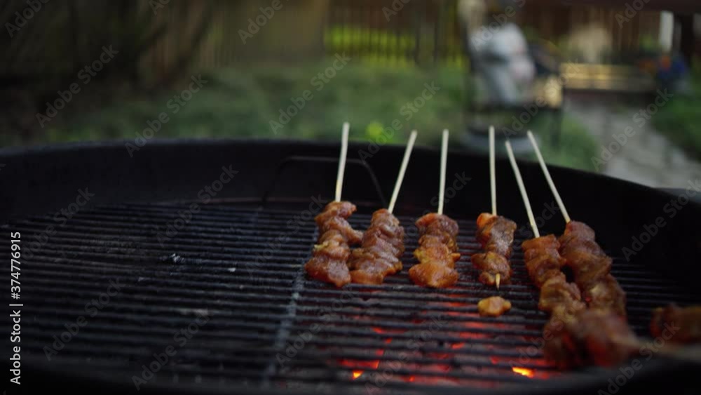 Indonesian woman grills chicken satay over charcoal in her back yard
