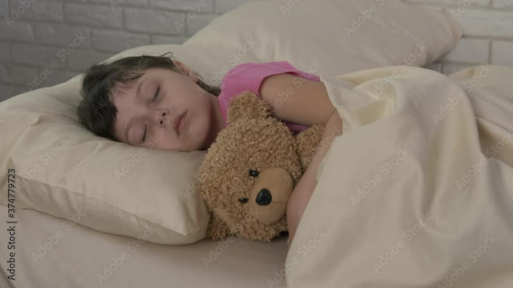 Relaxation with teddy bear. A cute little girl sleeps in bed hugging a teddy bear.