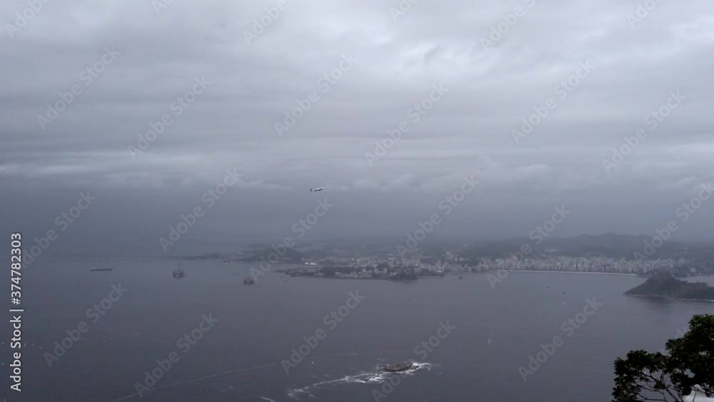 Scenic aerial view of Rio de Janiero landscape, ocean sea water and airplane flying above in grey overcast blanket of cumulus and stratus clouds on stormy cloud day, South America, handheld pan Scenic aerial view of Rio de Janiero landscape, ocean sea water and airplane flying above in grey overcast blanket of cumulus and stratus clouds on stormy cloud day, South America, handheld pan