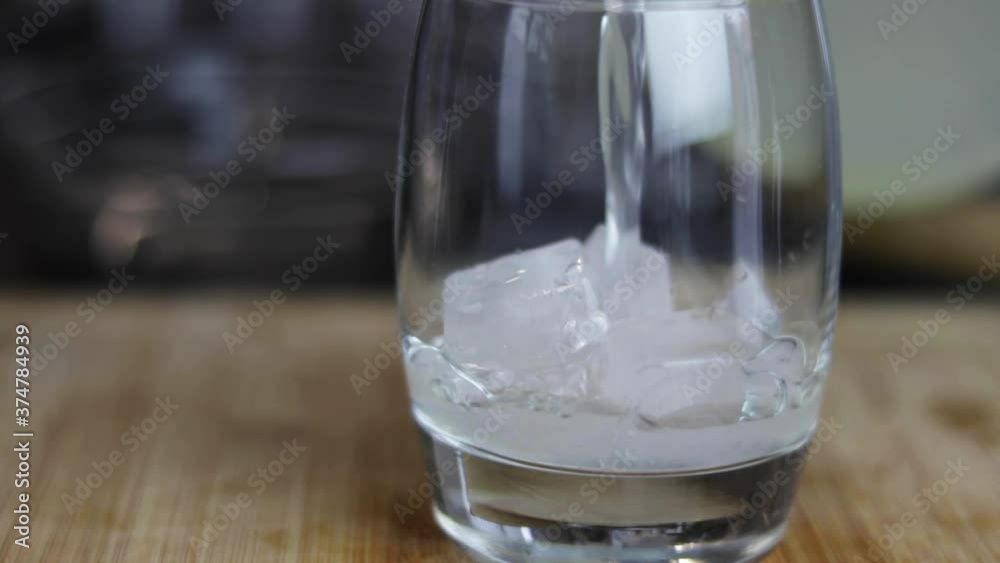 Slow motion shot of lemonade being poured into a glass, containing ice, which is sitting on a wooden board. Slow motion shot of lemonade being poured into a glass, containing ice, which is sitting on a wooden board.