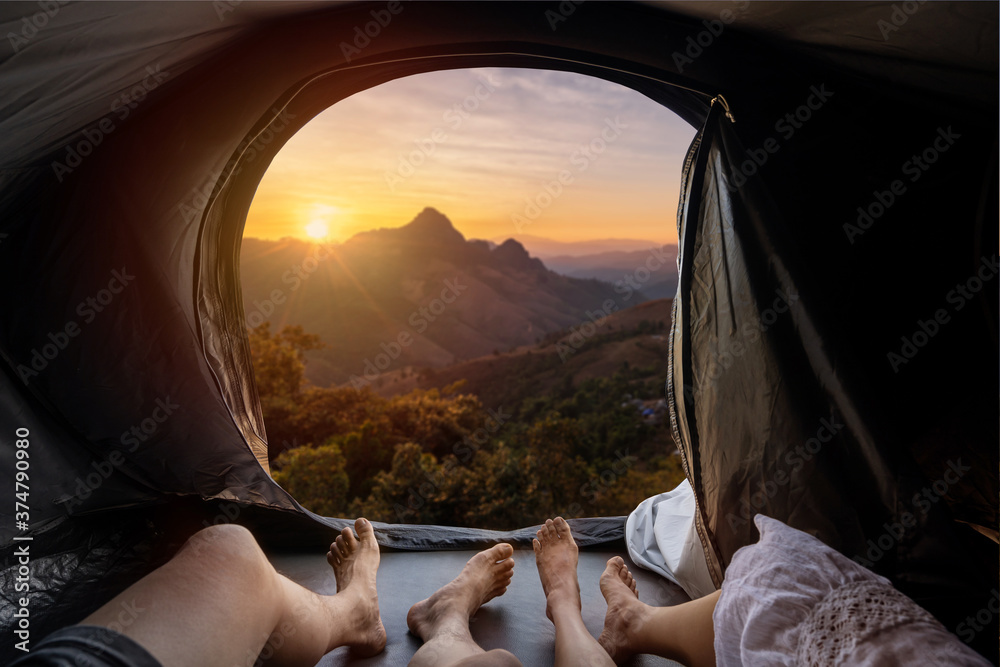 Young couple lying in camping tent and looking at sunset over the mountain