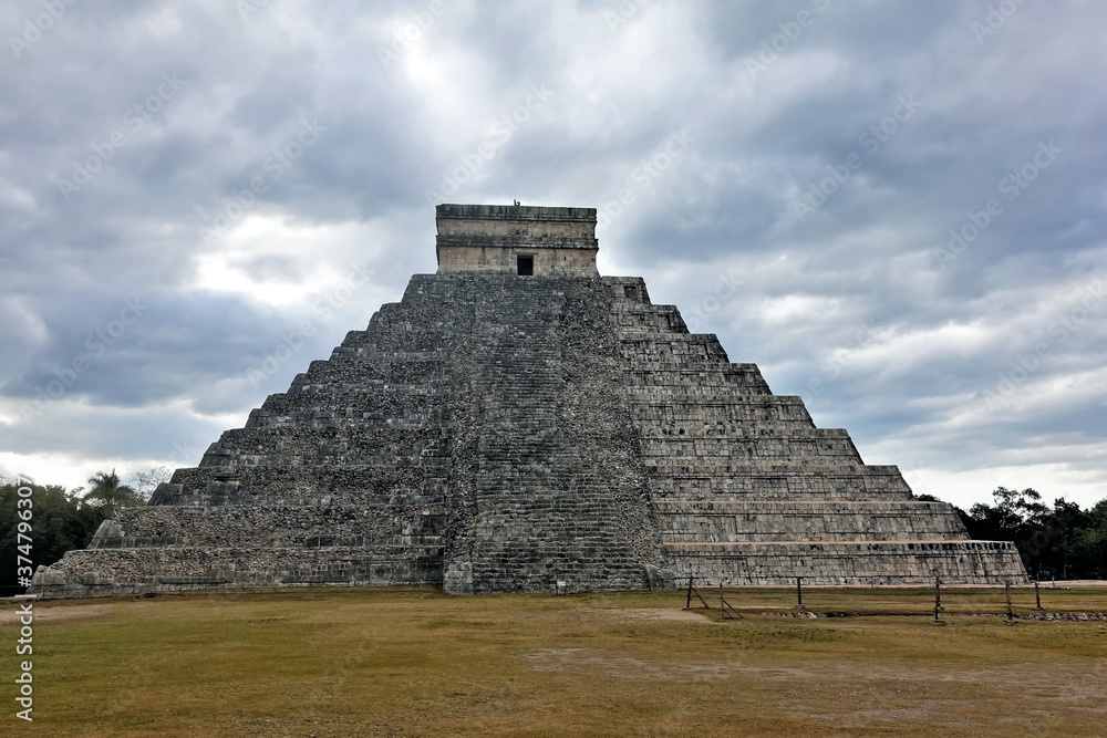 Unique pyramid of Kukulkan in the cloudy sky. An ancient stone ritual stepped building with a staircase. The left side has not been restored and looks dilapidated. Wonder of the World. Unesco heritage