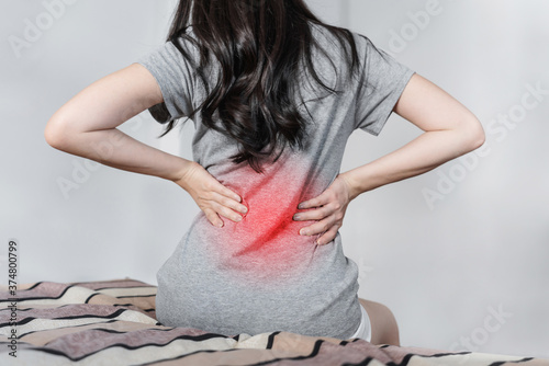 Backache and Lower back pain concept. Young woman suffering from back pain, on bed after waking up