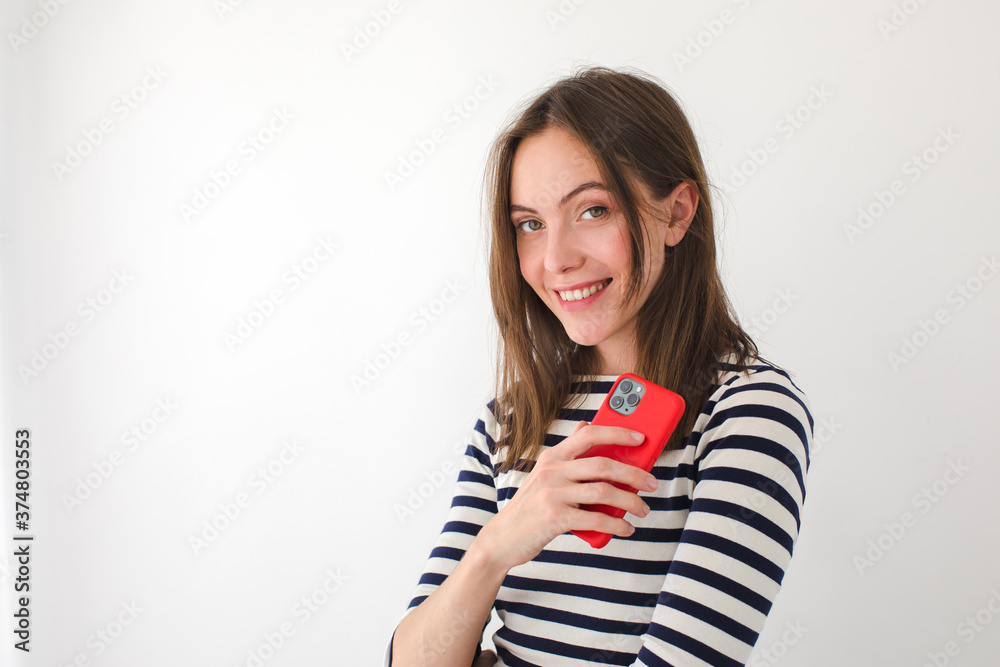 Cute female reading messages on cellphone and looking at camera while standing on a white background Cute female reading messages on cellphone and looking at camera while standing on a white background