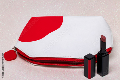 Table top on cosmetic background. Close-up of a beautiful opened red white cosmetic bag and an opened elegant red lipstick on a bright pink glittering background. Concept beauty. Macro.