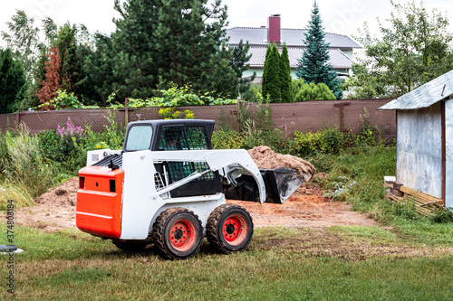A skid steer loader clears the site for construction. Land work by the territory improvement. Machine for work in confined areas. Small tractor with a bucket for moving soil and bulk materials.