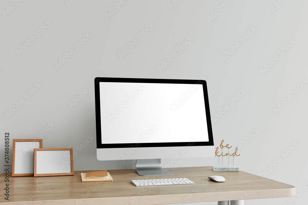 Modern PC monitor on table near light wall Modern PC monitor on table near light wall
