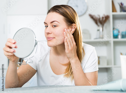 Cheerful woman is concentrared looking on her face in the mirror at the home.