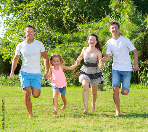 Cheerful family with two children having fun together, running in summer city park © JackF