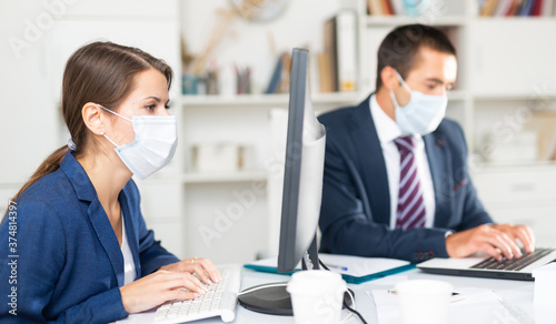 Portrait of young business woman focused on work with male colleague in office. People wearing medical face masks to prevent spread of viral infection
