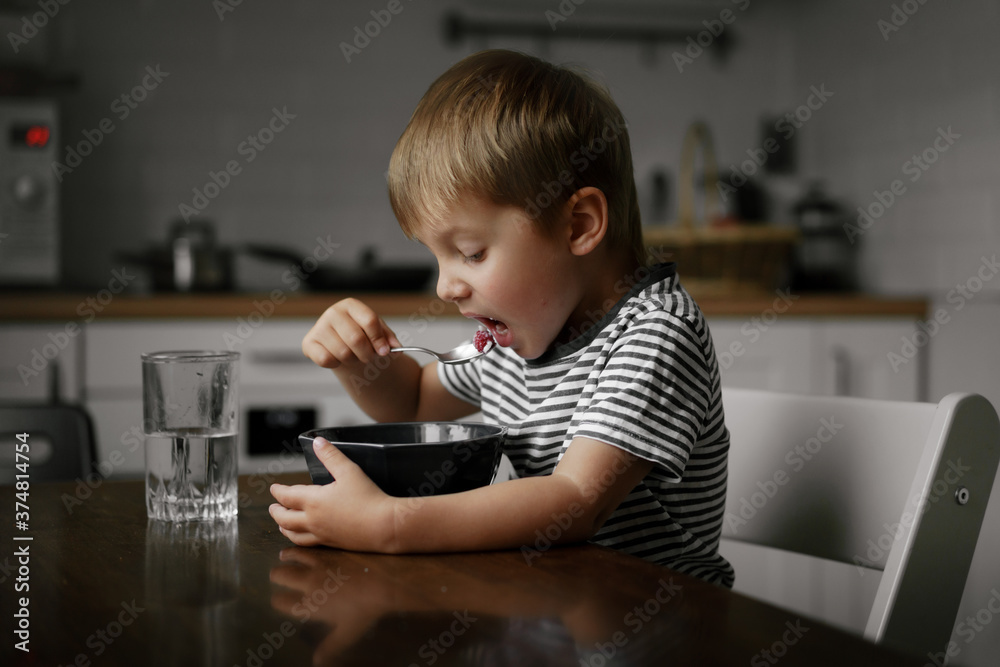 cute little boy putting spoon with porridge into his mouth, sitting at the table. Breakfast time. Image with selective focus cute little boy putting spoon with porridge into his mouth, sitting at the table. Breakfast time. Image with selective focus