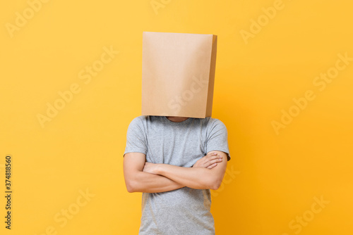Concept portrait of Anonymous man with head covered with paper bag doing arms crossed gesture in yellow studio background photo