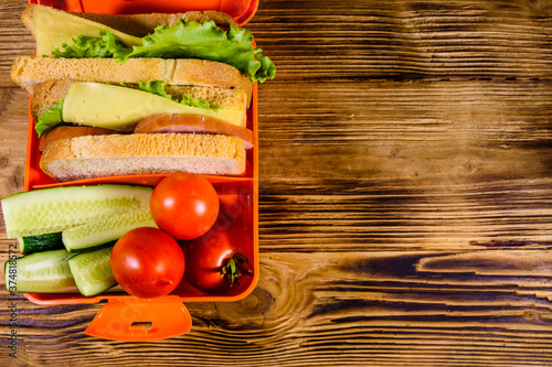 Lunch box with sandwiches  cucumbers and tomatoes on wooden table. Top view