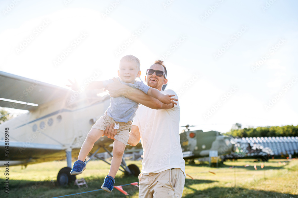 Obraz premium A dad and toddler spend time outdoors in an airplanes museum. A young father carries baby boy in hands like a airplane, they have fun together.
