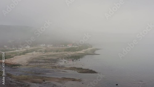 Extremely high bird's eeye view over shoreline as flock of birds fly off into distance on a foggy morning in a small fishing village photo