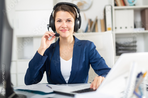 Smiling young female operator talking with customer using headset at company office