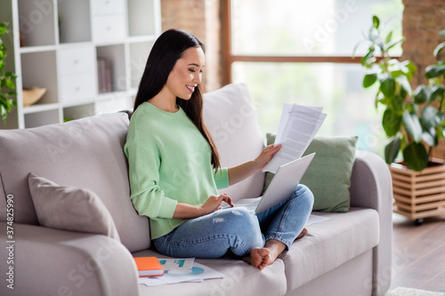 Full size profile side photo of smart asian manager expert girl sit divan legs crossed folded work remote use laptop focused read report in house indoors