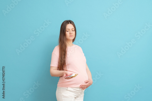 young beautiful pregnant woman on a blue background holding pills in her hand