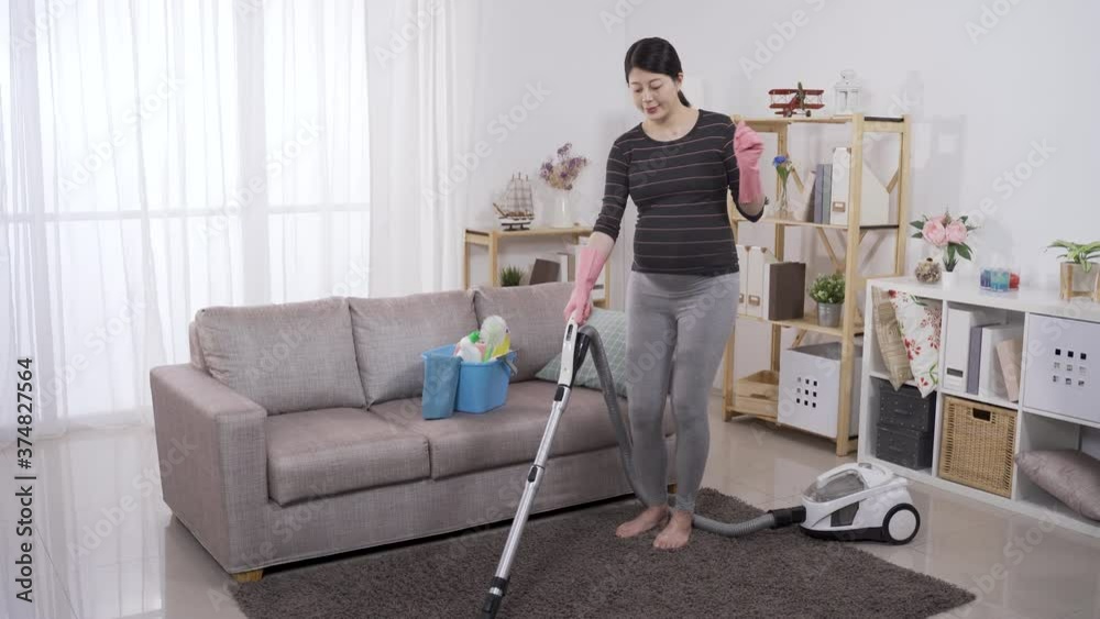expectant mother is dancing to music barefoot while using a vacuum cleaner to clean the rug in the living room. expectant mother is dancing to music barefoot while using a vacuum cleaner to clean the rug in the living room.