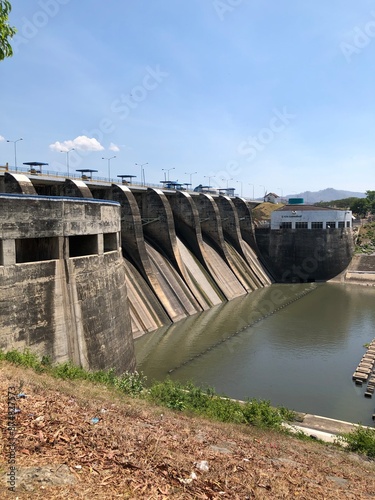 a water dam that stands firm and towers high, to accommodate and regulate the flow of river water from various directions, a dam that looks sturdy and majestic.