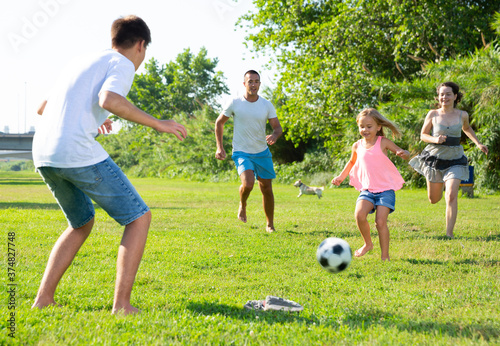 Young parents with theirs children having fun together outdoors, playing football on green grass