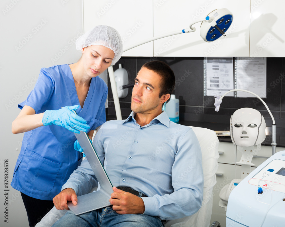 Obraz premium Skilled woman beautician examining face skin of young male patient before cosmetology procedure in beauty clinic