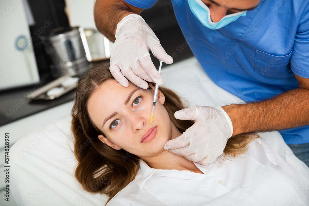 Portrait of young woman patient of beautician receiving rejuvenating facial injections