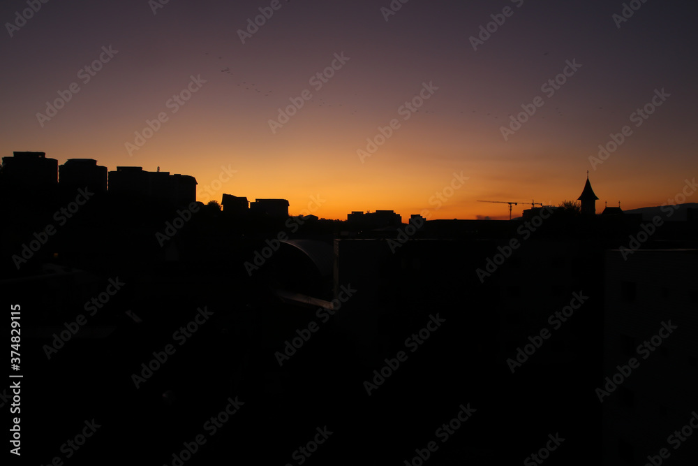 Orange sky during sunrise with silhouette buildings and city