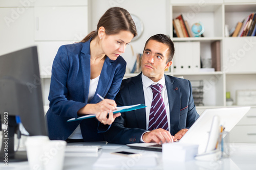 Confident businessman and female colleague working with papers and laptop in modern office