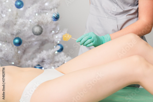 Young woman getting wax epilation of legs. Depilation concept. Product waxing bowl. Christmas discount waxing