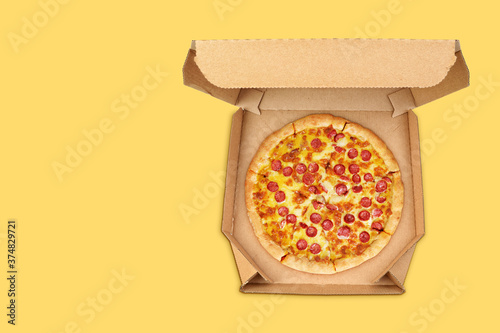 Pepperoni pizza in brown take-out box on yellow background. photo