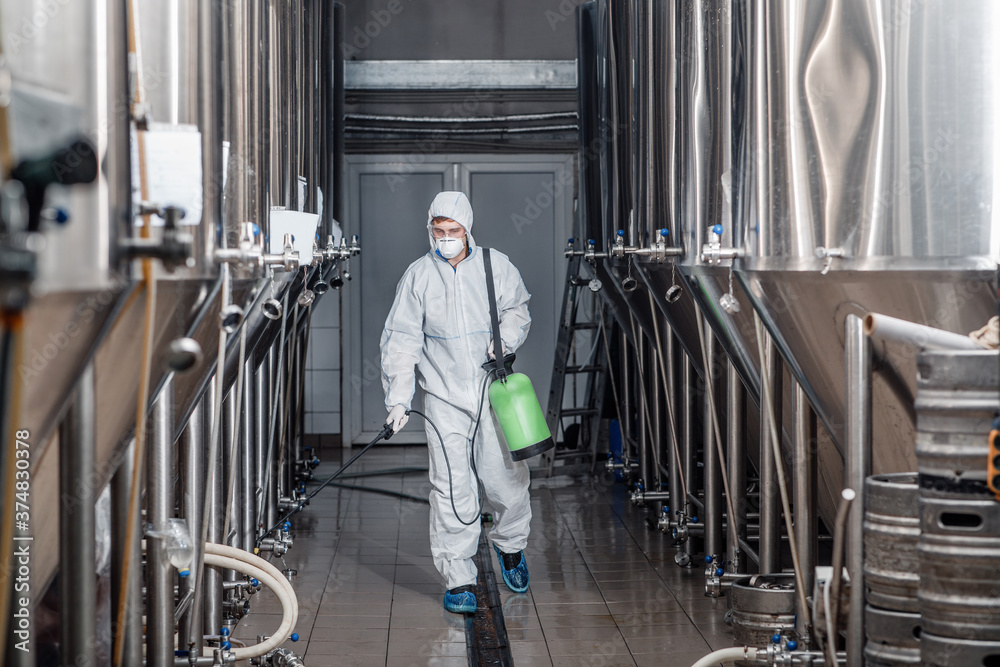 Brewer working with industrial equipment at brewery in protective suit and cleans up Brewer working with industrial equipment at brewery in protective suit and cleans up