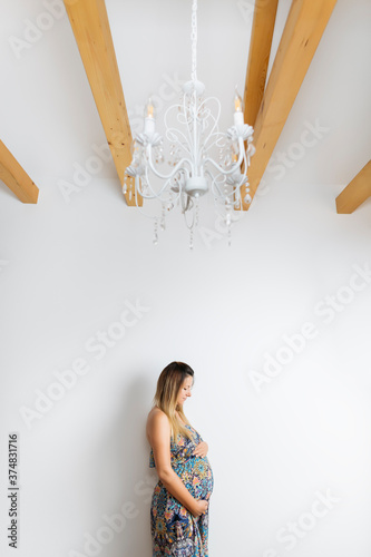 Beautiful pregnant woman in colorful dress on white background. Her arms are all around belly.