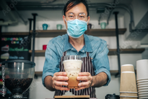 Business woner man wearing face mask for good hygiene coffee shop owner serving ice coffee young entrepreneur,friendly waitor with glasses smiling holding and serving. photo