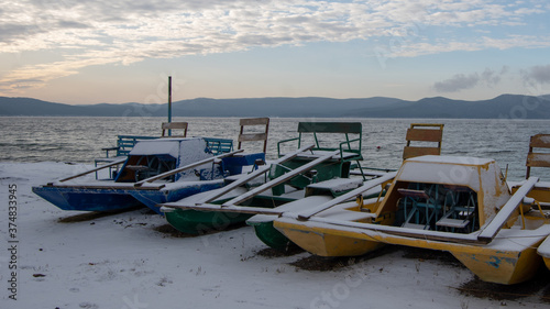 Landscape of a winter lake with multi-colored catamarans in a frozen lake and mountains