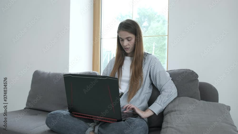 smiling young woman sitting on couch, using laptop notebook, looking at screen, typing message, happy lady chatting on computer, browsing, surfing internet, studying, writing or working online at home smiling young woman sitting on couch, using laptop notebook, looking at screen, typing message, happy lady chatting on computer, browsing, surfing internet, studying, writing or working online at home