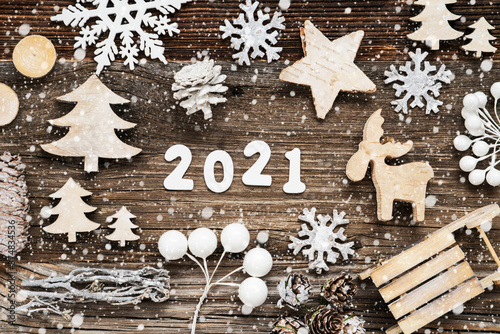 White Letters Building The Word 2021. Wooden Christmas Decoration Like Seld And Tree And Star. Brown Wooden Background With Snowflakes