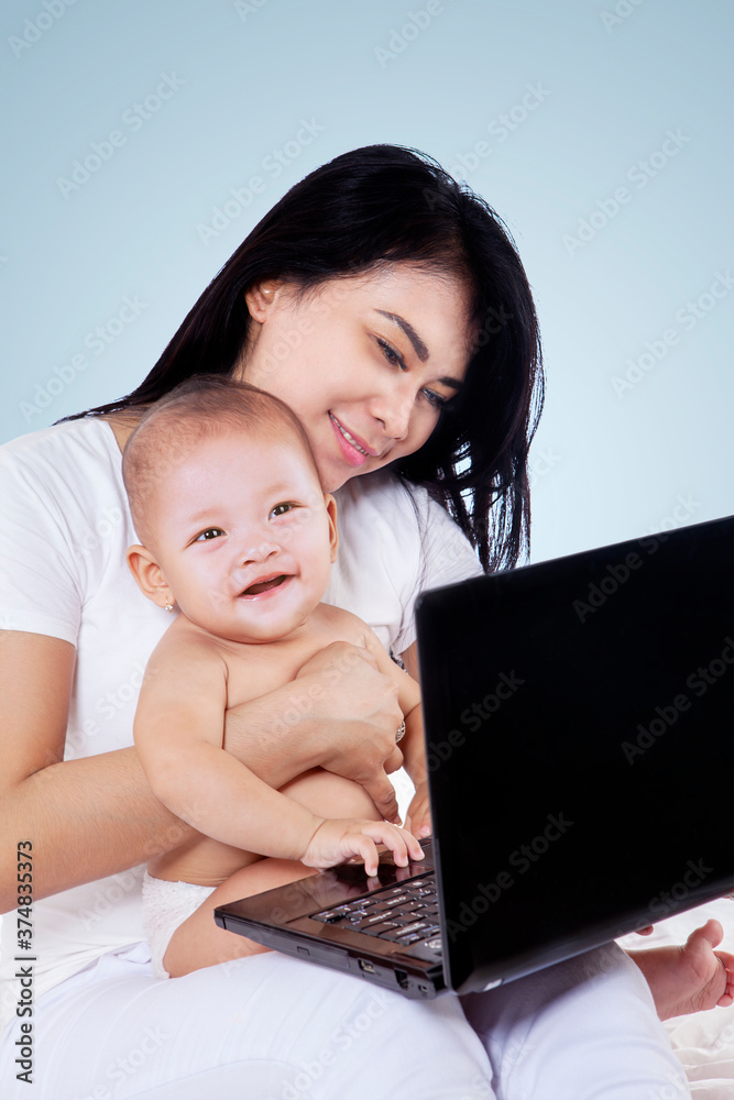 Mother holds her baby while using a laptop on studio Mother holds her baby while using a laptop on studio