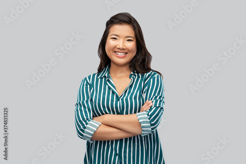 people, ethnicity and portrait concept - happy asian young woman with crossed arms over grey background