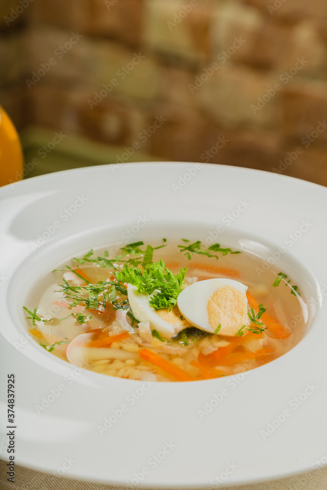 Fresh soup with vegetables, meat and eggs in a white plate.