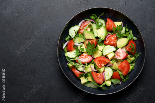 Avocado salad with tomatoes, cucumbers, parsley and arugula. Balanced nutrition concept. Black stone background