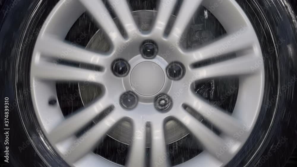 A car wheel with a shiny silver rim rides in the rain drops, turns to the right, to the left and strong shaking on bad road. Closeup. Slow mo, slo mo, slow motion, high speed camera